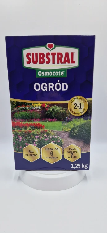 Front: Duże opakowanie nawozu uniwersalnego Substral Osmocote Ogród z widokiem na kwitnący ogród i krzewy.